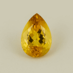 Golden yellow pear-cut topaz gemstone on a neutral background, showing brilliant facets and warm autumnal tones.