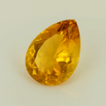 Golden-yellow pear-cut citrine gemstone on a neutral background, showing brilliant facets and high clarity under soft studio lighting.