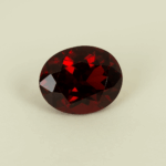 Deep red oval-cut garnet gemstone on a neutral background, showcasing brilliant facets and rich color under soft studio lighting.